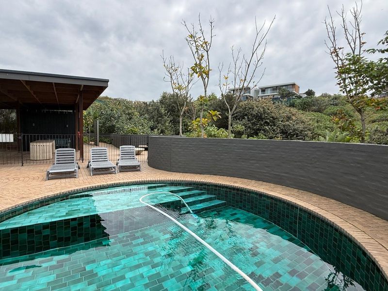 A well-maintained outdoor pool area featuring a tiled swimming pool, paved surround, and a covered patio space for relaxation.