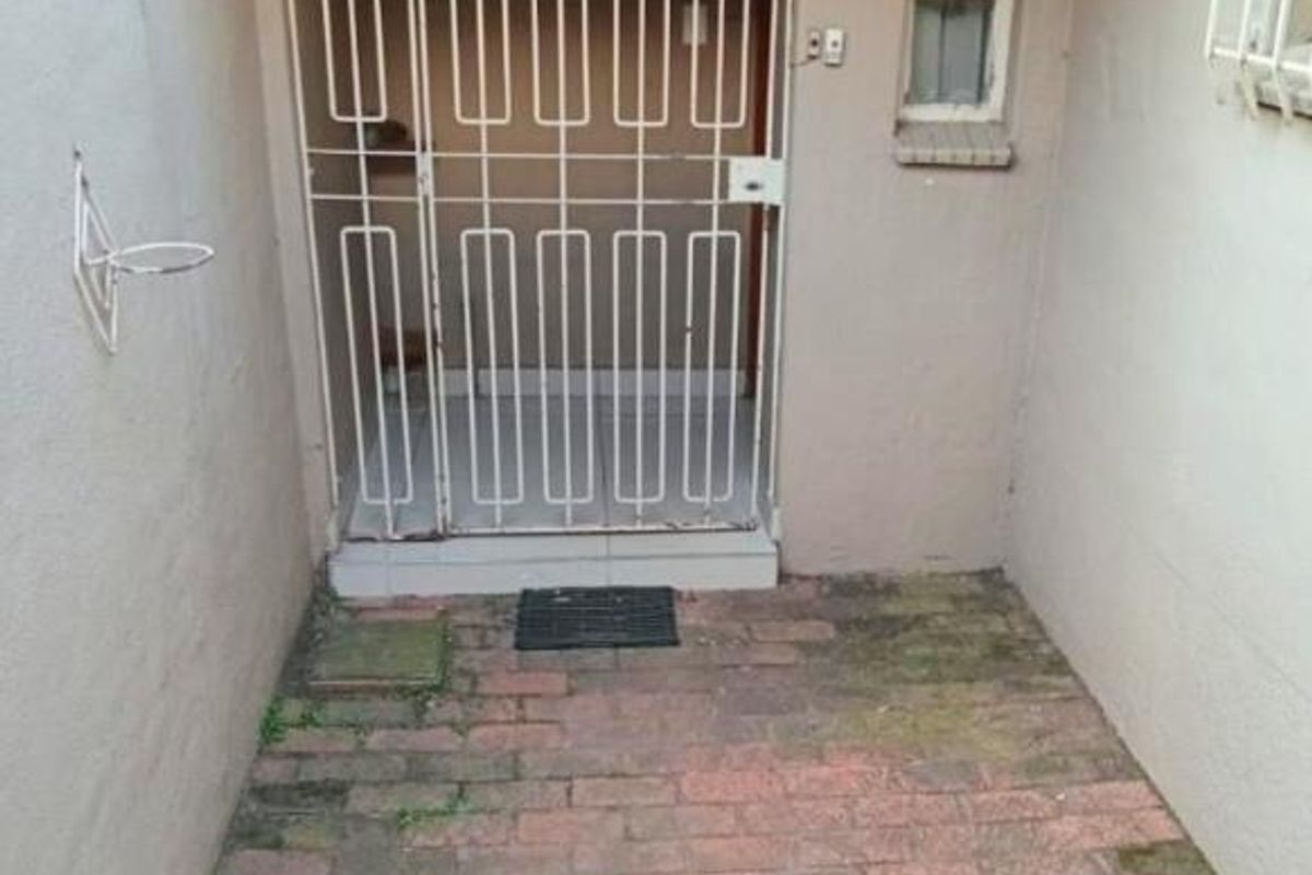 A small rear courtyard area featuring brick paving, a security gate entrance, and a protective awning over the doorway.