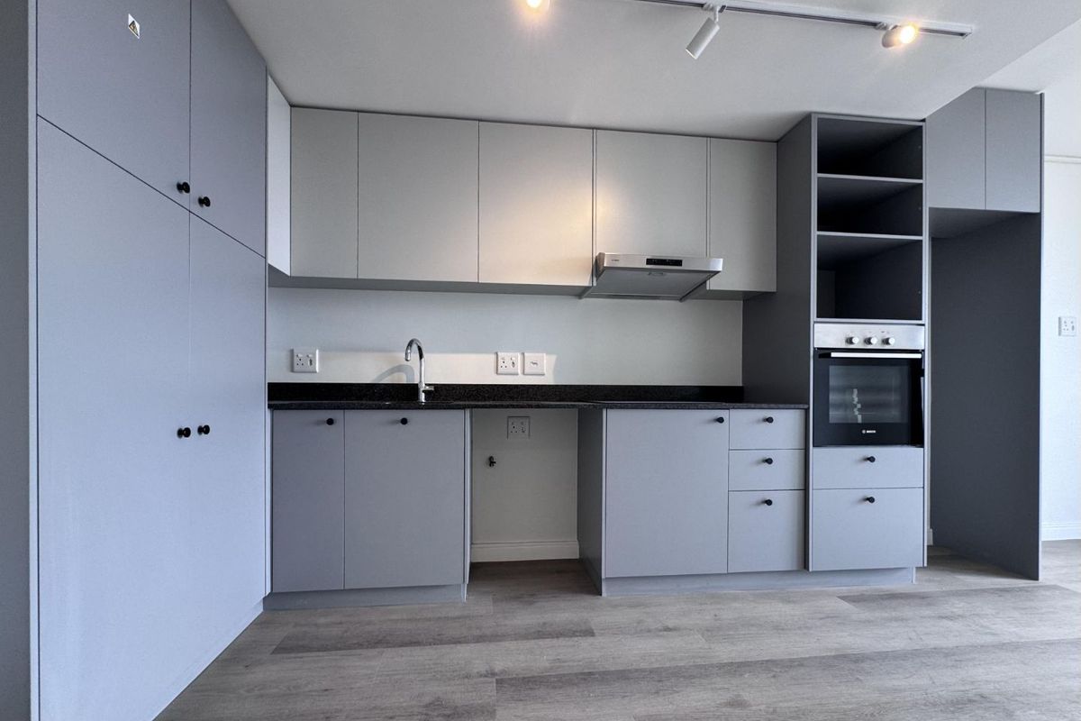 Modern kitchen featuring sleek grey cabinetry, stone countertops, built-in oven, extractor fan, and high-quality laminate flooring in a clean, contemporary design.