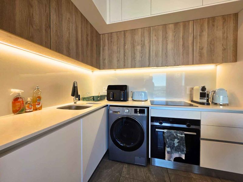 Modern kitchen featuring sleek wood-grain and white cabinetry, stone countertops, integrated appliances, and ambient under-cabinet lighting.