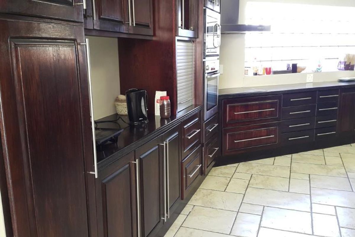 A kitchen featuring dark wood cabinetry, integrated oven and microwave, dark countertops, and light-colored tiled flooring with a glass block window.