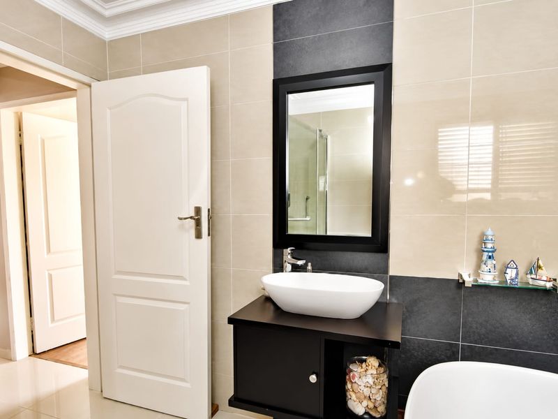 A modern bathroom featuring a vessel sink on a dark vanity cabinet, contrasting wall tiles, and a framed mirror.
