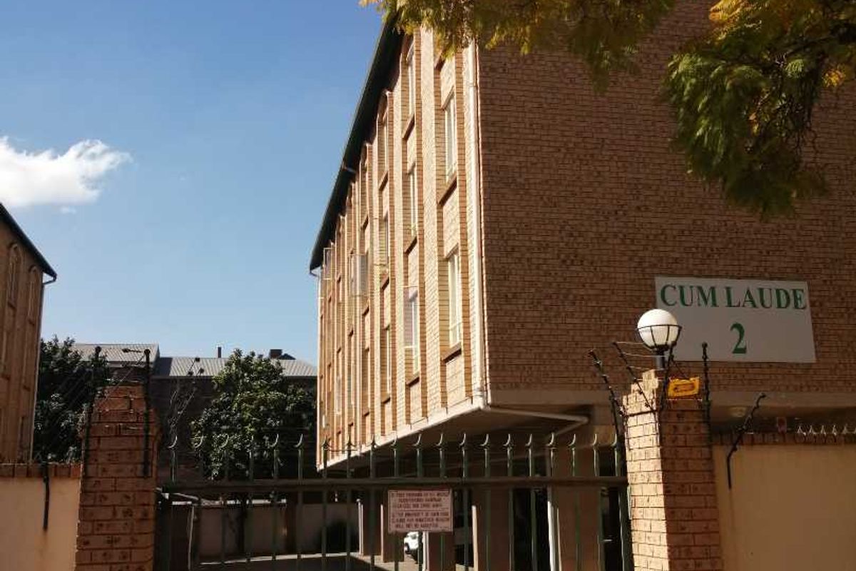 Exterior view of the Cum Laude apartment complex featuring a brick facade, secure gated entrance, and paved driveway access.