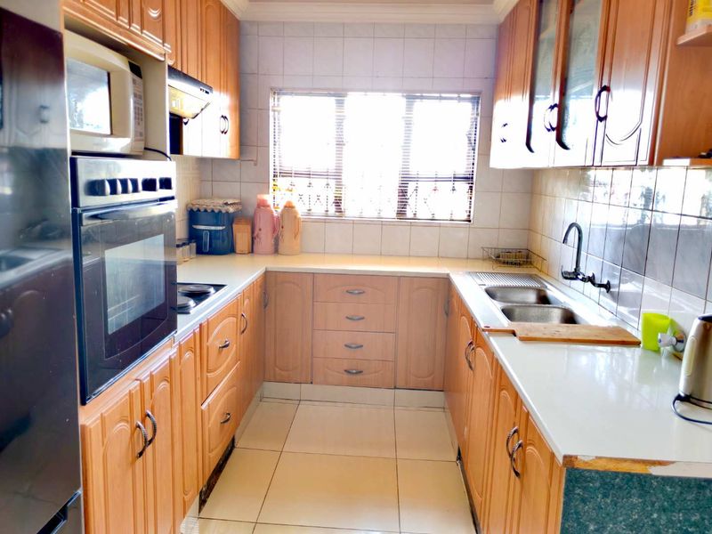 A functional U-shaped kitchen featuring wood-finish cabinetry, built-in oven, hob, extractor fan, and a double sink with tiled backsplash and flooring.