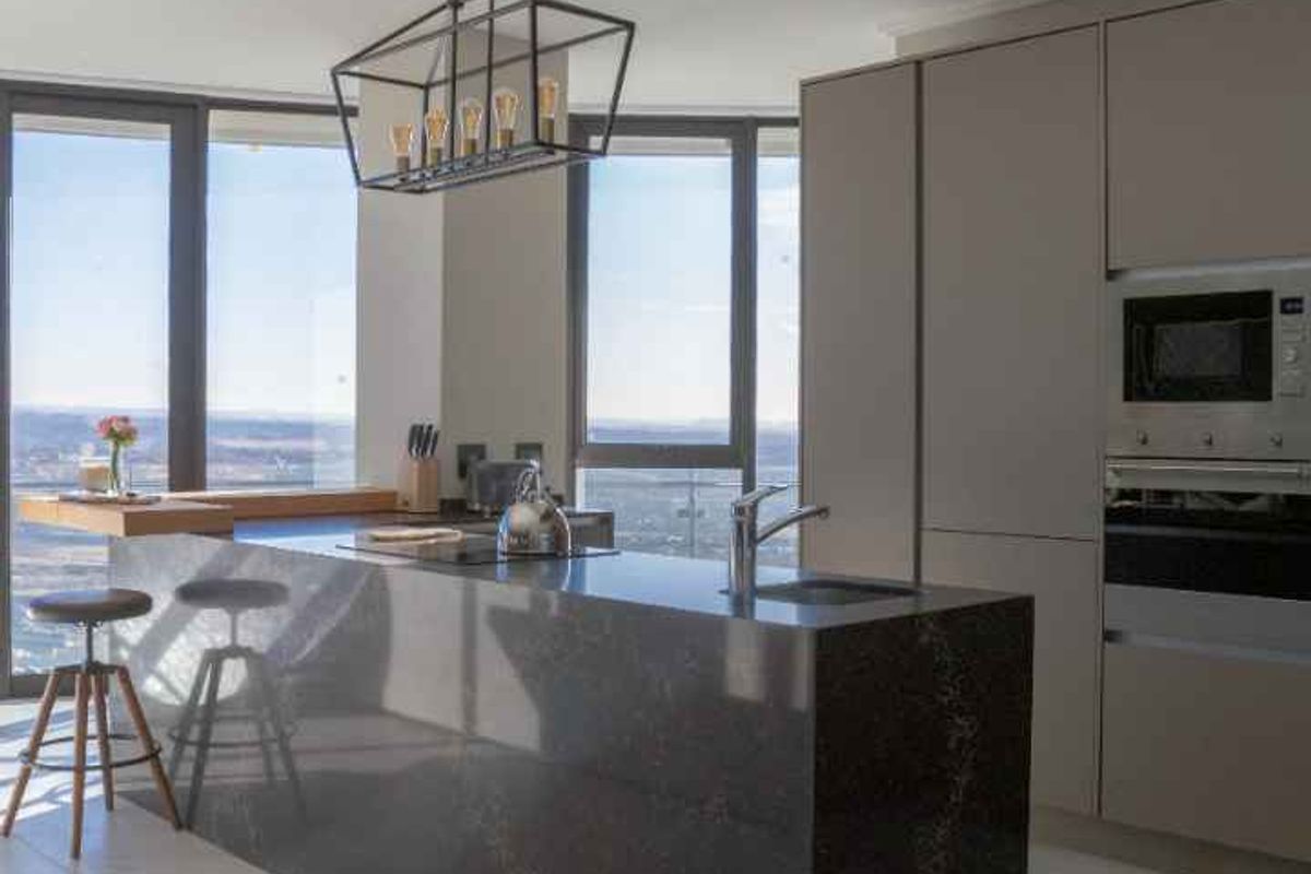 Modern penthouse kitchen featuring a sleek stone island, integrated appliances, and floor-to-ceiling windows offering expansive views.