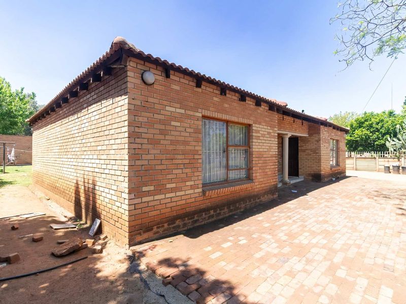 Rear view of a face brick house featuring a paved patio area, exposed roof rafters, and secure window bars.