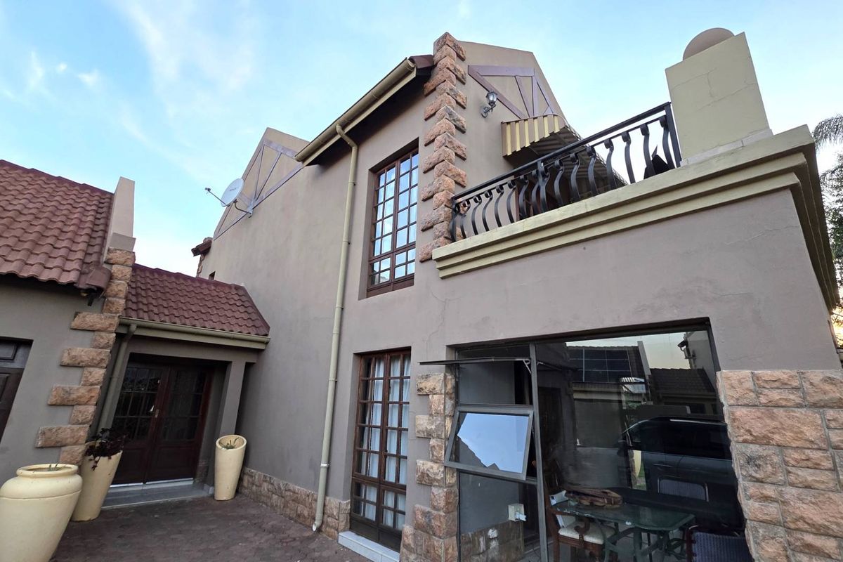 Rear elevation of a multi-story house featuring stone cladding, a balcony with wrought iron railings, and tiled roofing.