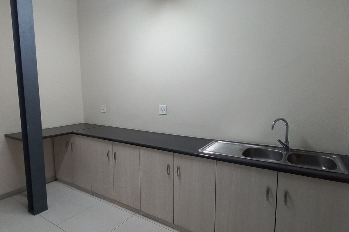 A functional kitchenette area featuring light wood cabinetry, a dark laminate countertop, and a stainless steel double sink with a mixer tap.