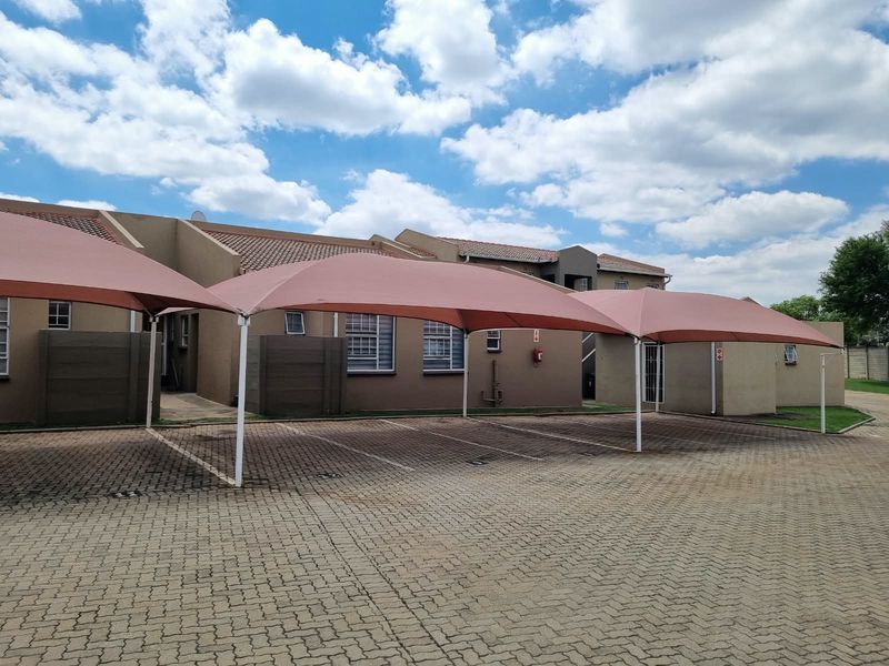 Exterior view of the townhouse complex featuring paved parking bays with shade cloth carports and well-maintained building facades.