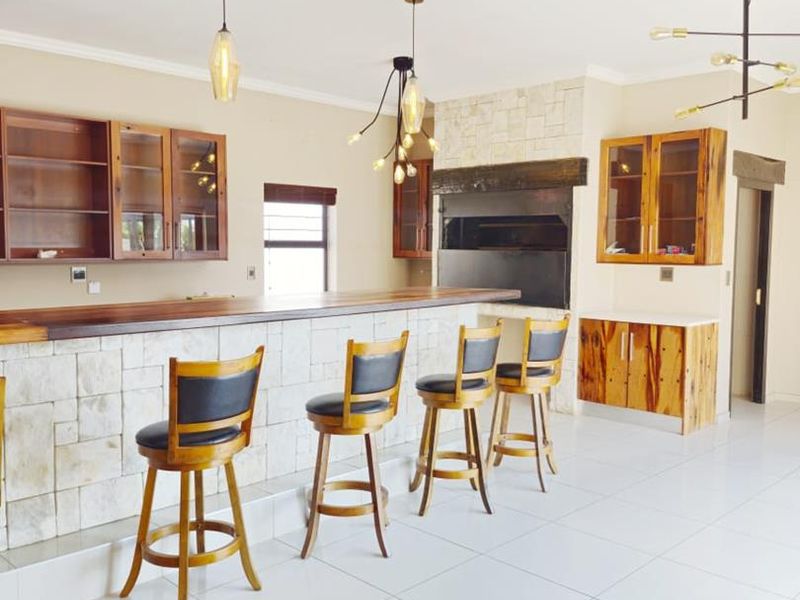 A well-appointed indoor bar area featuring a stone-clad counter, built-in braai, wooden cabinetry, and modern pendant lighting with clean tiled flooring.