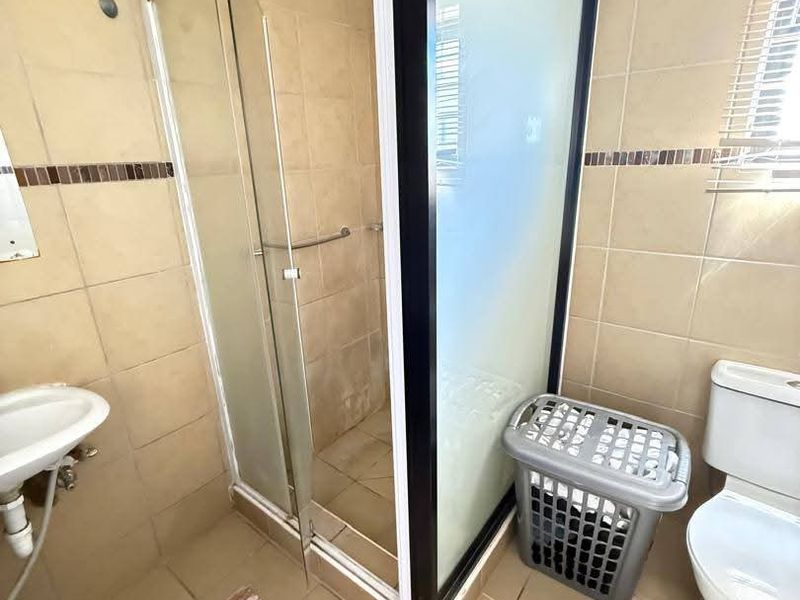 A functional bathroom featuring a shower enclosure, toilet, and basin with neutral wall and floor tiling.