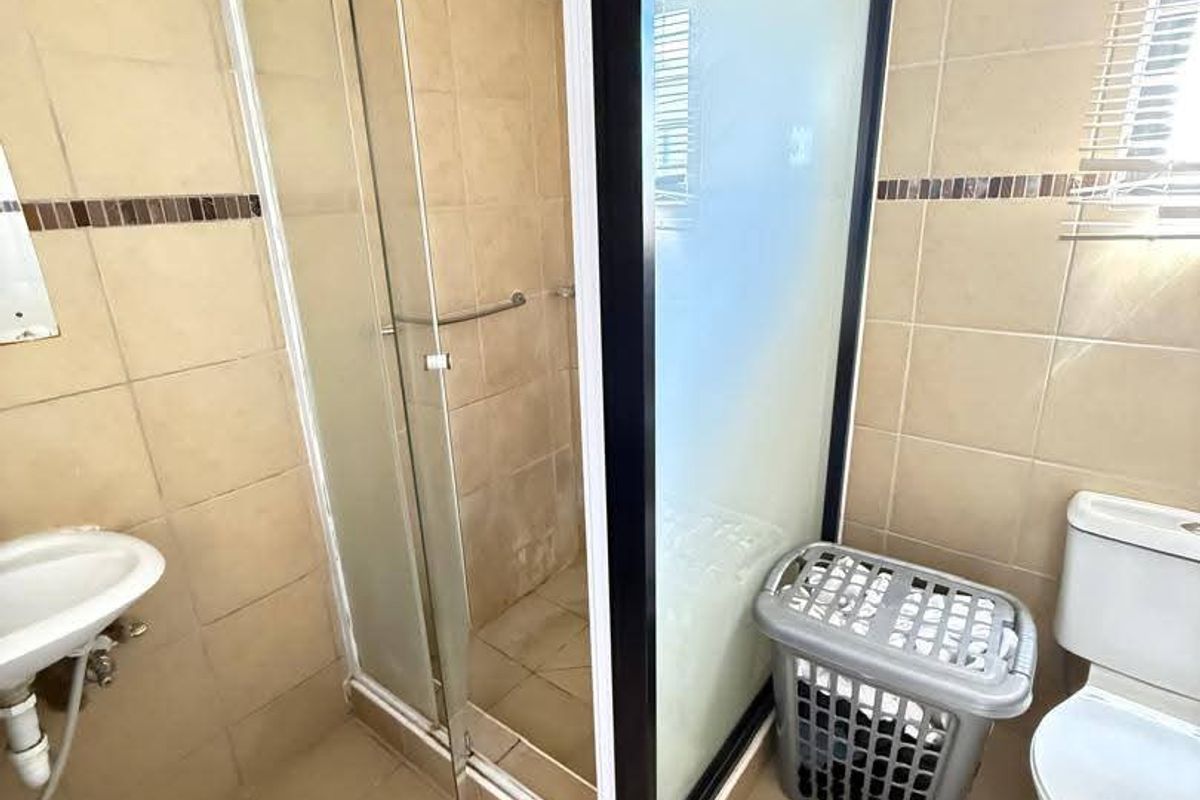 A functional bathroom featuring a shower enclosure, toilet, and basin with neutral wall and floor tiling.