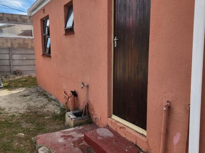 Rear exterior view of the property featuring a timber door, concrete step, and external plumbing fixtures against a painted masonry wall.