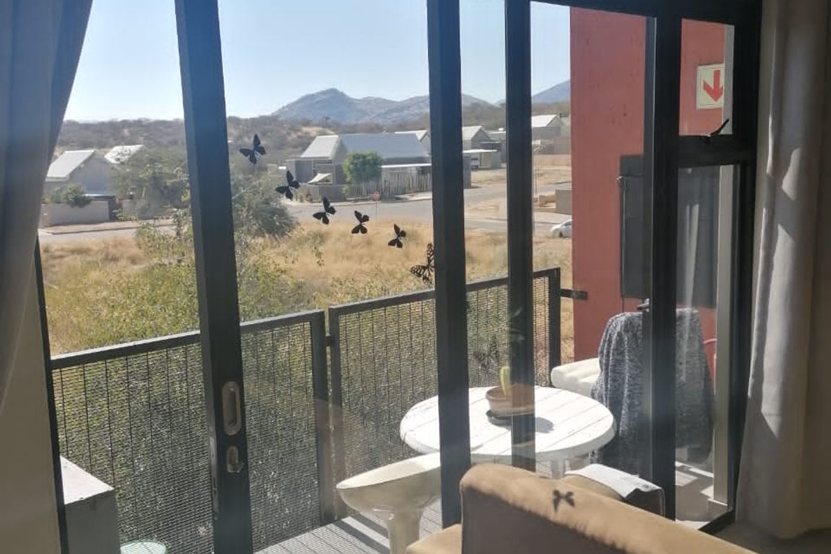 A balcony featuring a metal mesh balustrade and sliding glass door access, offering views of the surrounding neighbourhood and distant hills.