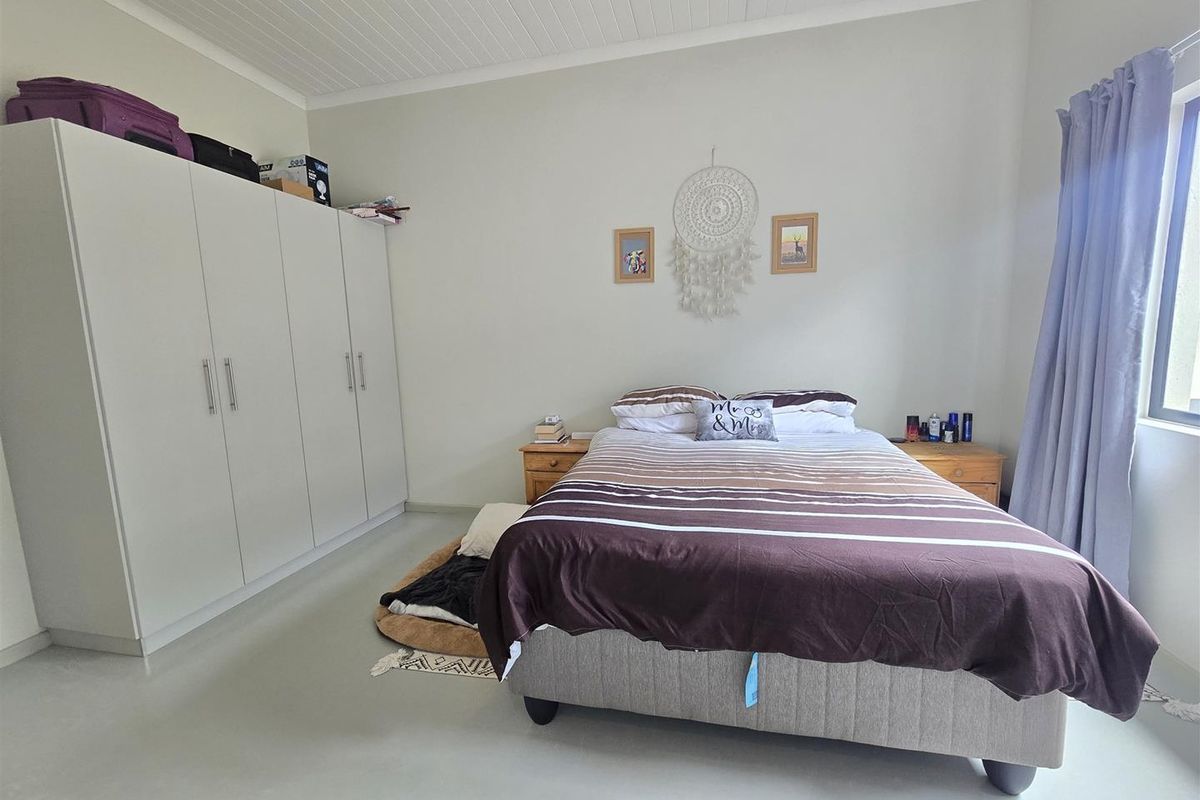 A well-lit bedroom featuring built-in floor-to-ceiling wardrobes, neutral painted walls, and a white tongue-and-groove ceiling.