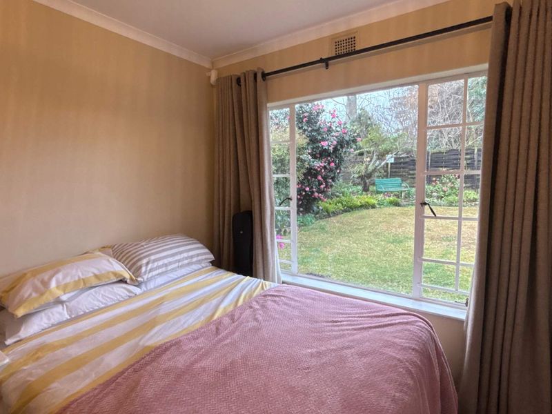A cozy bedroom featuring a large window with garden views, neutral wall tones, and classic coving detail.