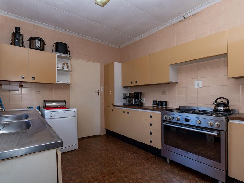 A functional kitchen featuring dated laminate cabinetry, a stainless steel double sink, gas stove, and tiled splashbacks, offering potential for modern renovation.