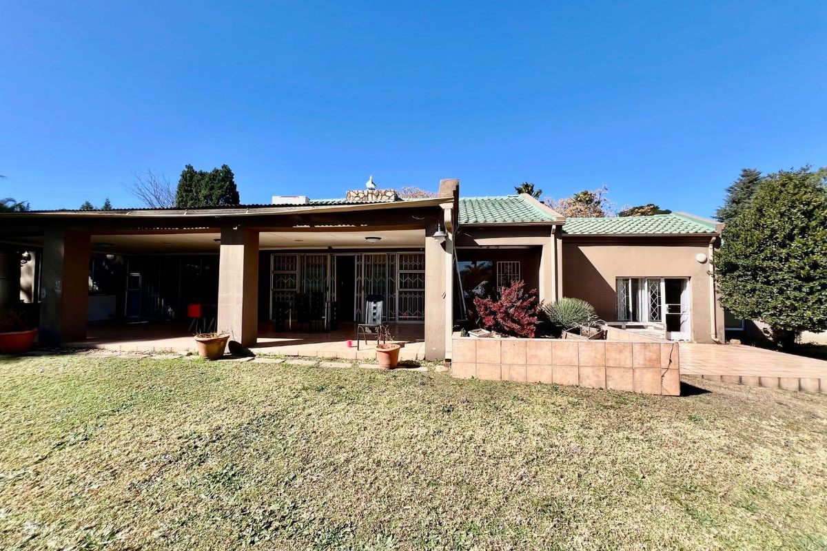 Rear view of the house featuring a covered patio, paved outdoor space, and a garden area with a brick retaining wall.