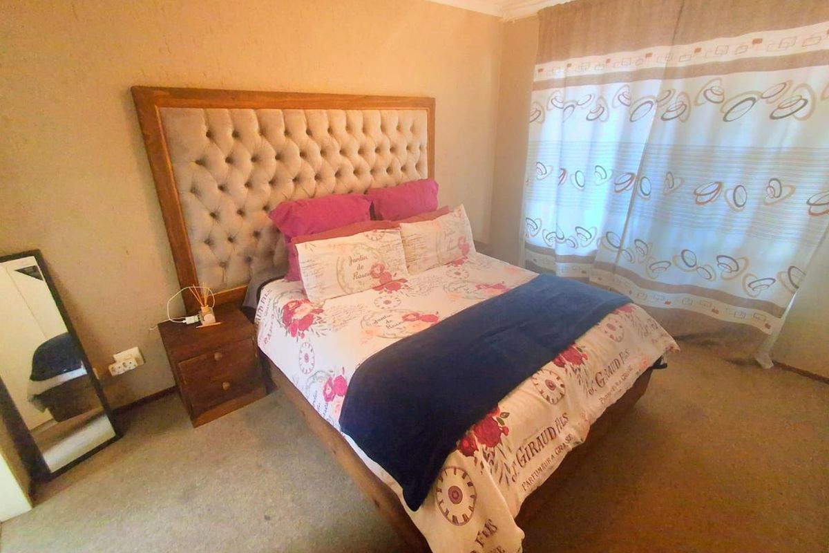 A bedroom featuring neutral wall tones, carpeted flooring, and a large window with curtains.