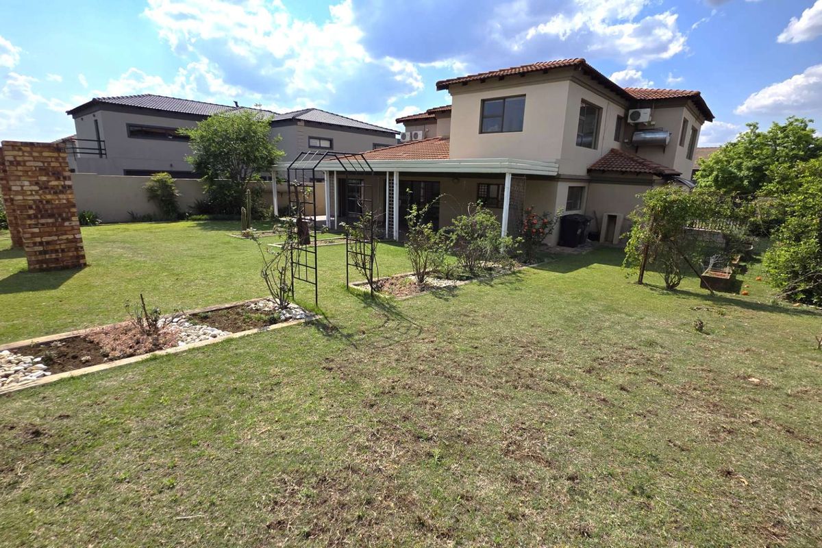 Rear view of the house featuring a spacious garden, covered patio area, and established landscaping with a brick pillar and metal garden arch.
