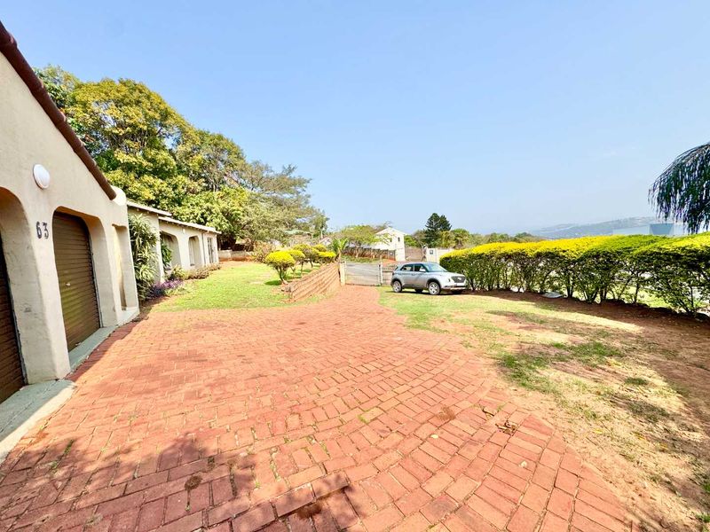 Front exterior view of the property featuring a brick paved driveway, garage access, and a landscaped garden area with a retaining wall.
