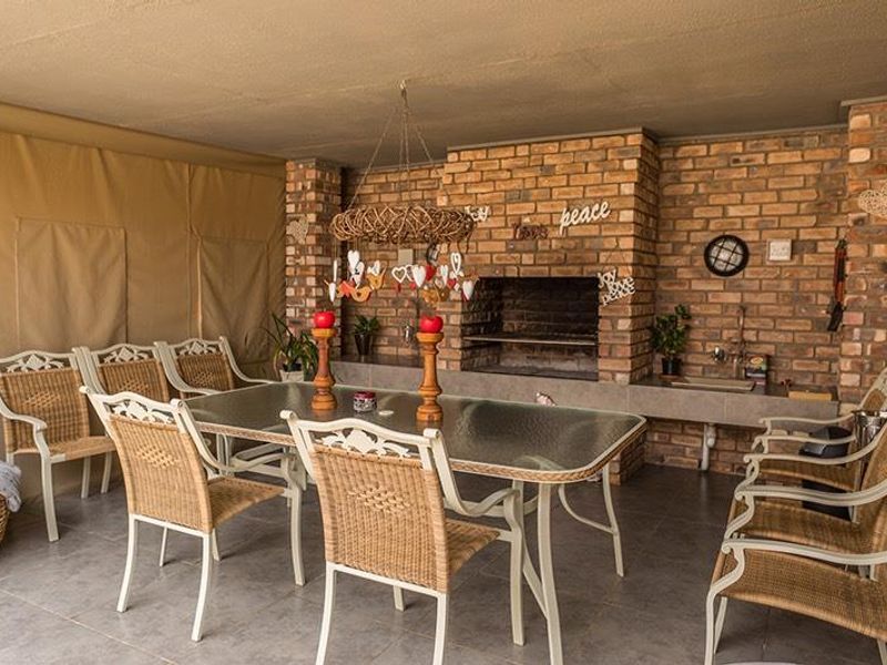 A spacious covered patio featuring a built-in brick braai, prep sink, and durable tiled flooring, ideal for outdoor entertaining and dining.