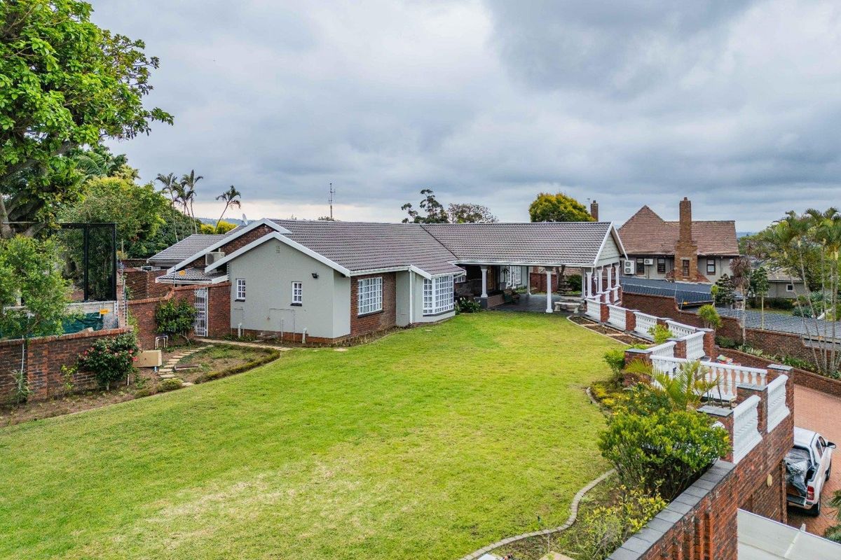 Rear view of the property featuring a spacious lawn, covered patio area, and established brick boundary walls with decorative balustrades.