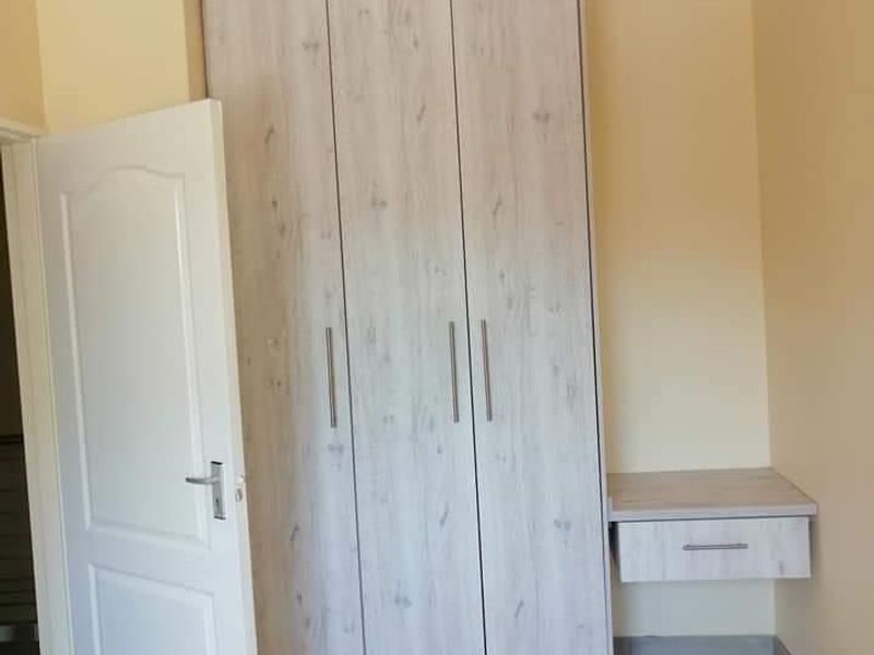 A clean bedroom featuring a modern light wood-grain built-in wardrobe with an integrated floating vanity desk and neutral tiled flooring.