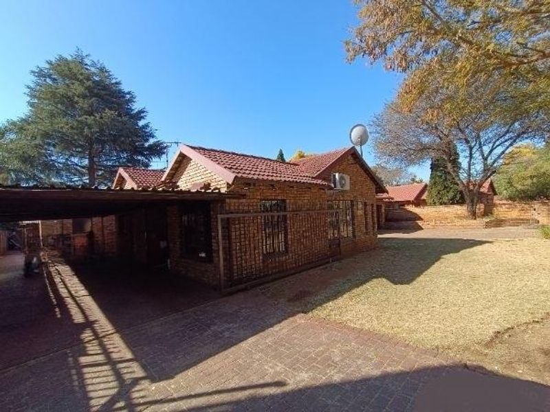 A single-story face brick house featuring a tiled roof, attached carport, paved driveway, and established garden area.