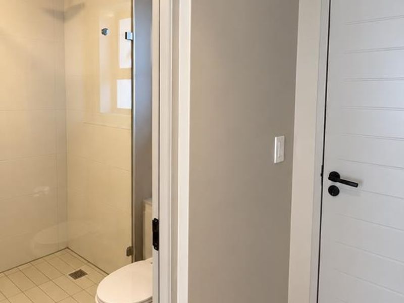 A modern, clean bathroom featuring a walk-in shower with a rain shower head, glass screen, and neutral tiled flooring.
