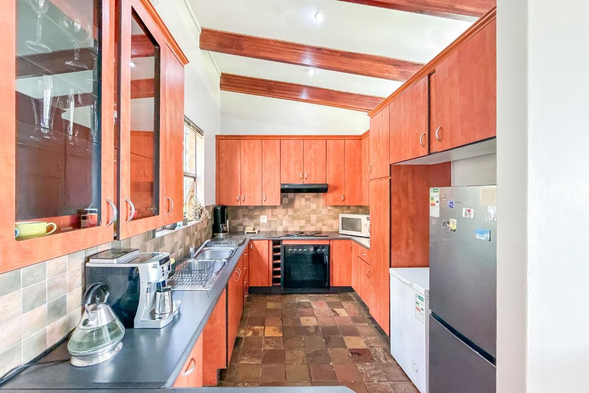 A functional kitchen featuring wooden cabinetry, exposed ceiling beams, tiled flooring, and built-in cooking appliances.