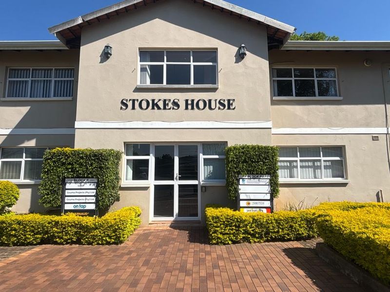 Front facade of Stokes House, a well-maintained commercial office building featuring paved access, manicured hedges, and aluminium-framed windows.