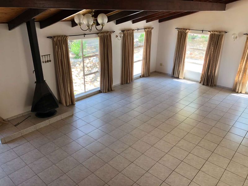 Spacious living area featuring exposed timber ceiling beams, tiled flooring, and a prominent freestanding fireplace, offering a bright and open layout.