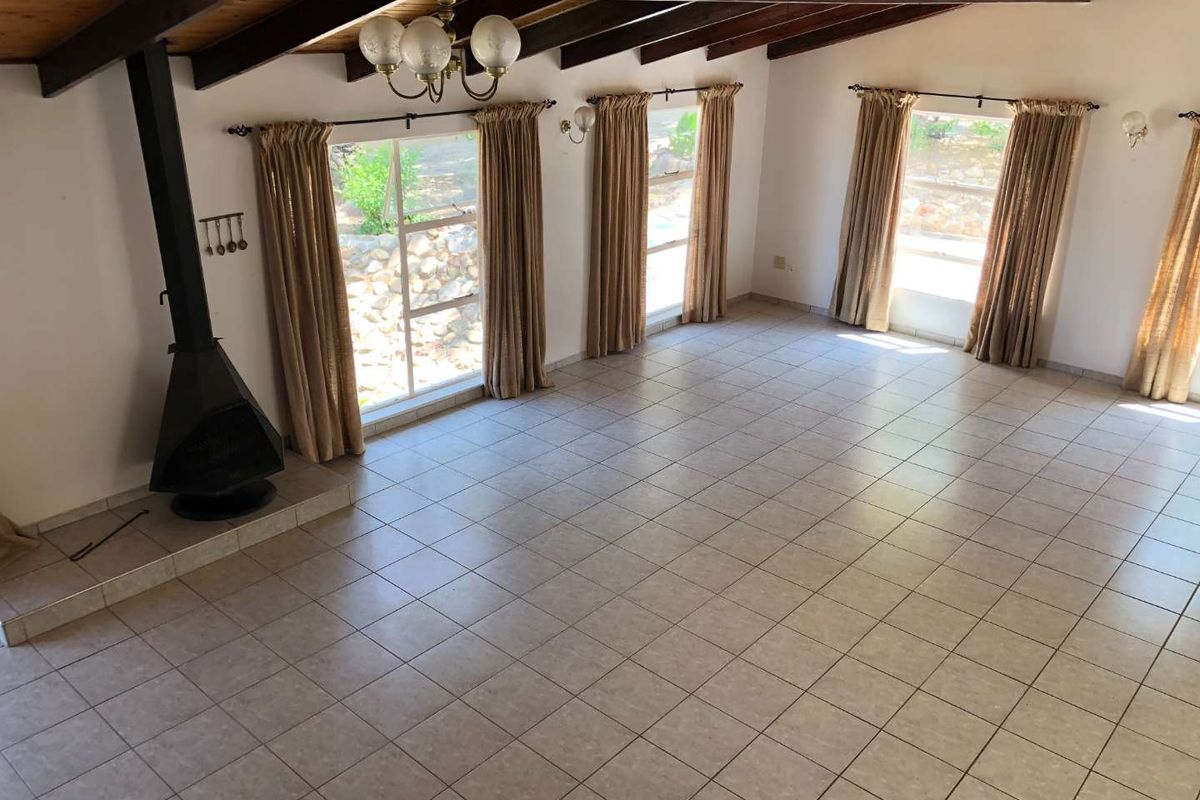 Spacious living area featuring exposed timber ceiling beams, tiled flooring, and a prominent freestanding fireplace, offering a bright and open layout.