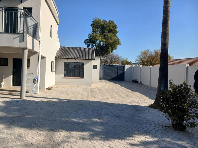 Rear exterior view of the property featuring a paved driveway, boundary wall, metal gate, and a balcony overlooking the yard area.