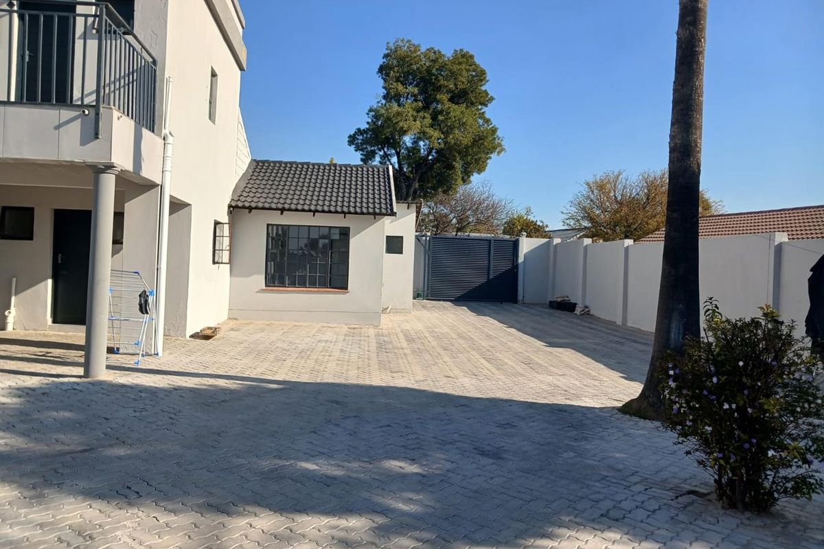 Rear exterior view of the property featuring a paved driveway, boundary wall, metal gate, and a balcony overlooking the yard area.