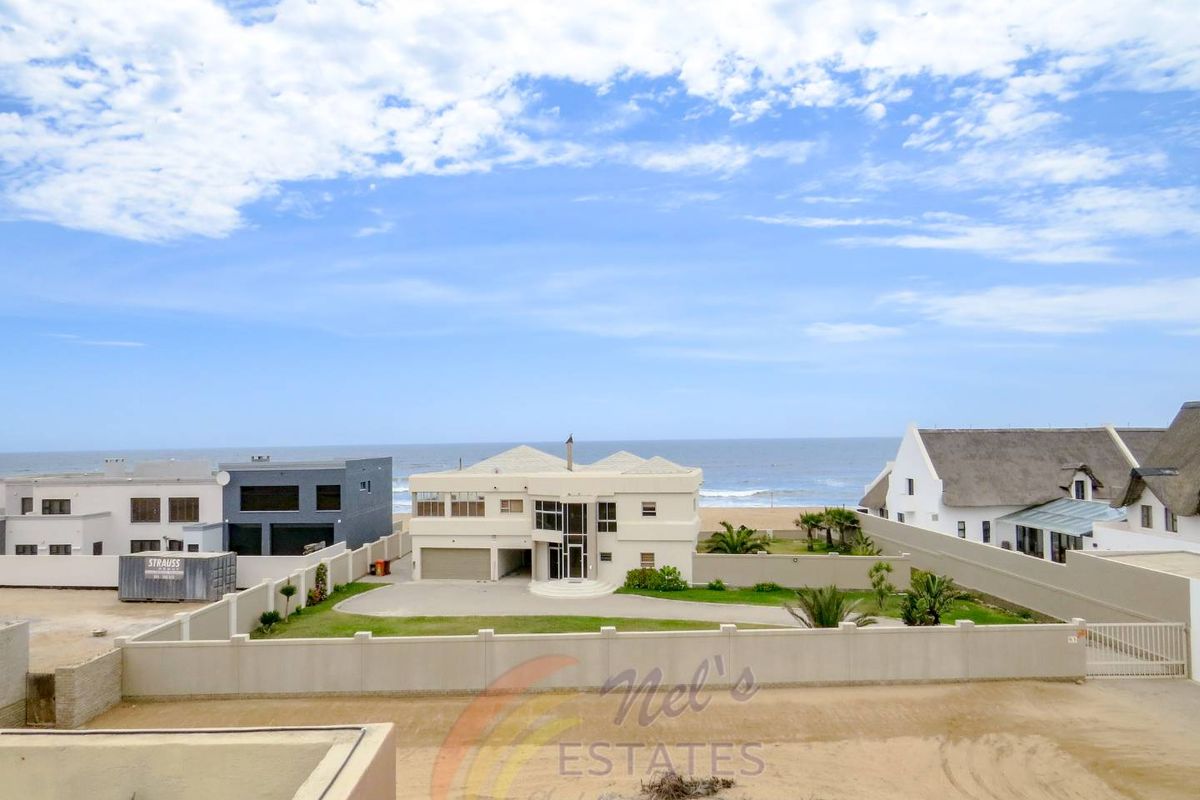 Aerial view of a beachfront property featuring a paved driveway, perimeter wall, and direct access to the coastline.