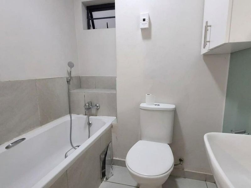 A functional bathroom featuring a bathtub with handheld shower, toilet, and wall-mounted storage cabinet, requiring minor repairs to the bathtub panel.