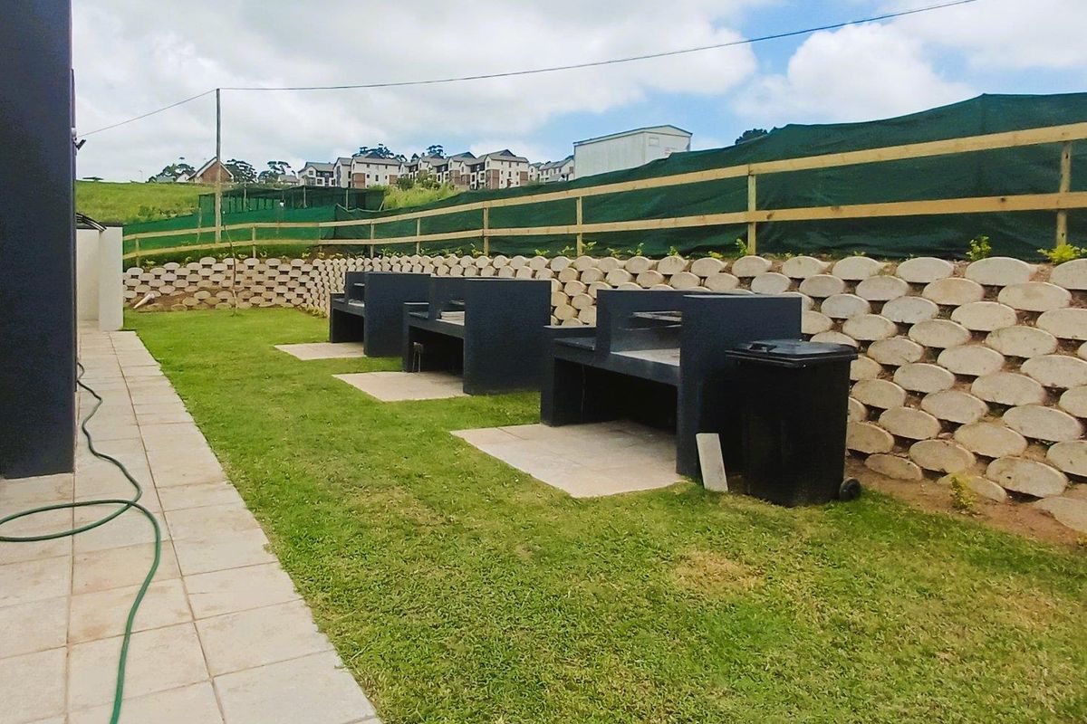 Outdoor communal area featuring multiple built-in brick braai stands, paved walkways, and a tiered retaining wall in a residential townhouse complex.