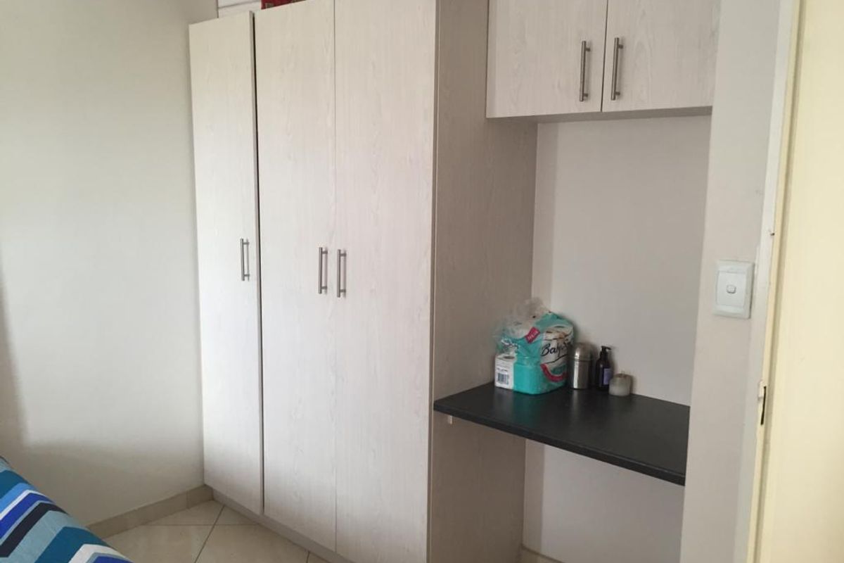 Bedroom featuring a light wood-grain built-in wardrobe with integrated desk space and overhead storage cabinets, complemented by tiled flooring.