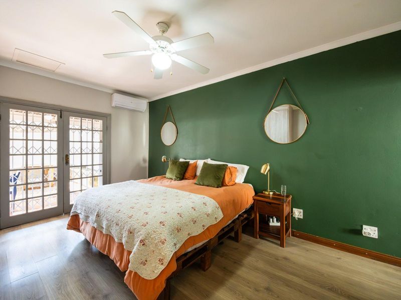 A well-maintained bedroom featuring laminate flooring, a ceiling fan, split-system air conditioning, and direct access to an outdoor area through glass-paned french doors.