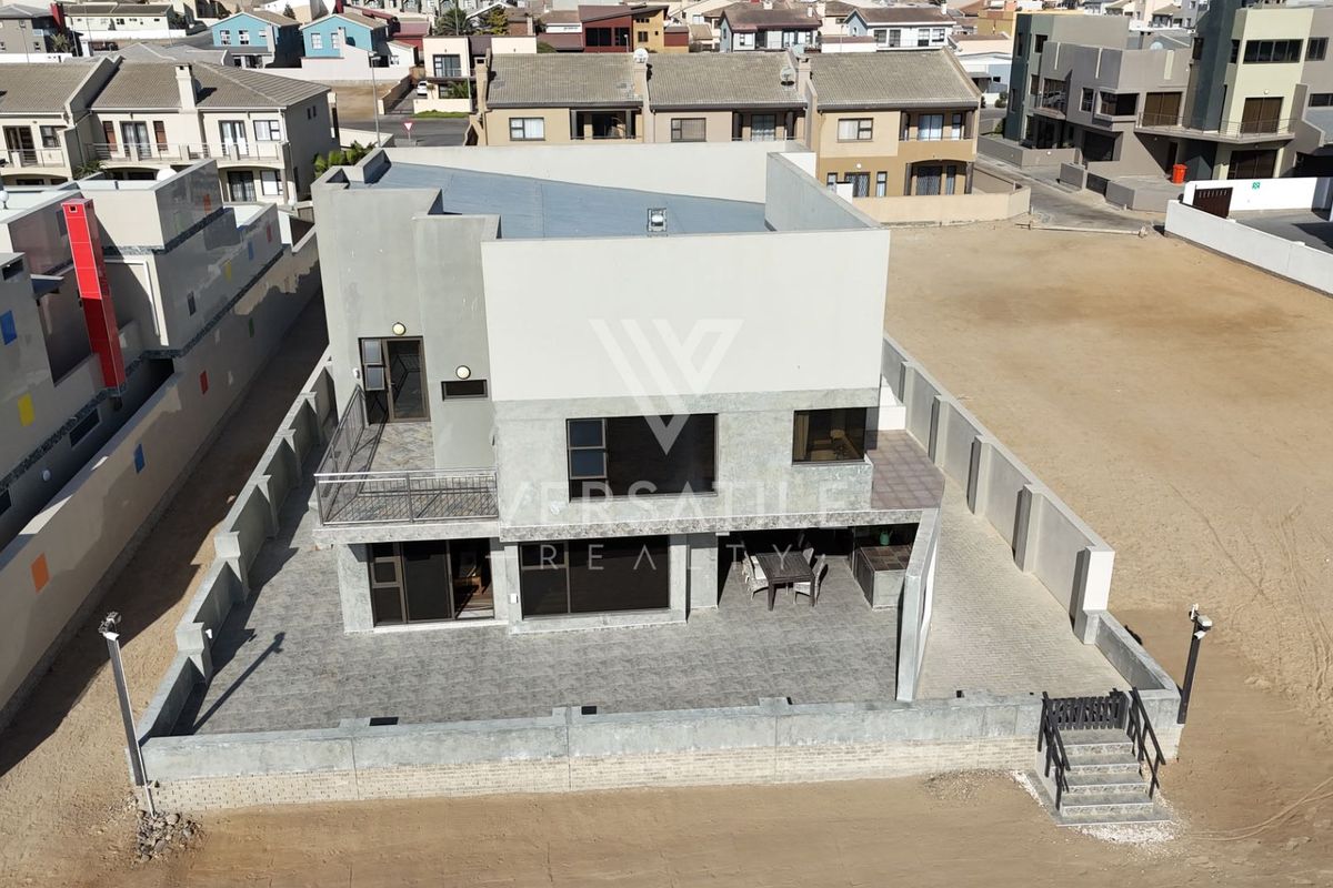 Aerial view of a modern two-story residential property featuring a paved courtyard, balcony, and perimeter boundary walls in a suburban estate setting.