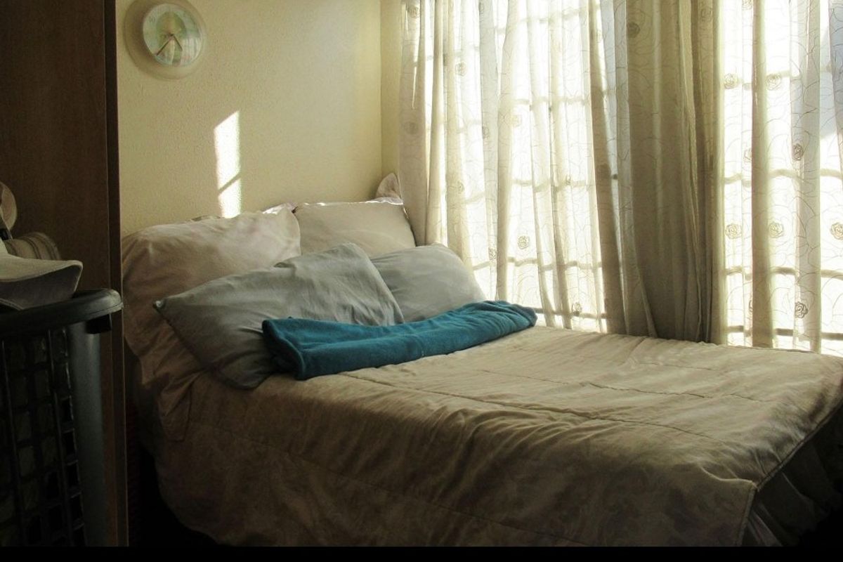 A bedroom featuring natural light through glass-paned doors, providing a simple and functional sleeping space.