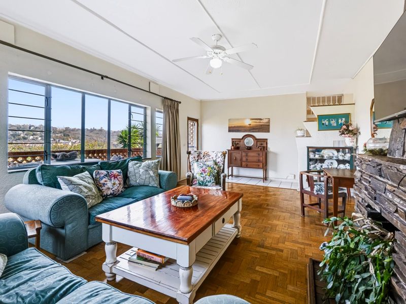 Spacious living room featuring classic parquet flooring, a prominent stone fireplace, and large windows offering natural light and scenic views.