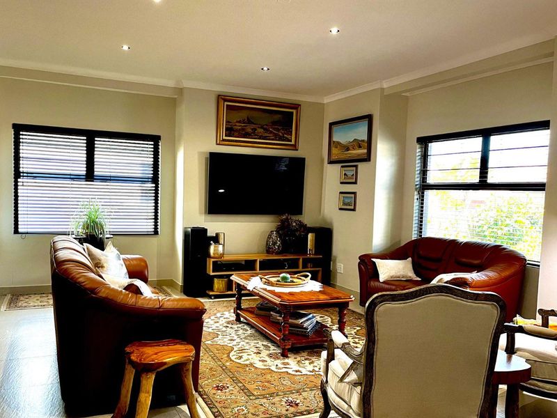 A well-maintained living room featuring tiled flooring, recessed downlights, and large windows with modern aluminium frames and venetian blinds.