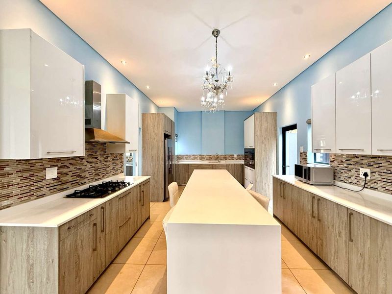 Modern kitchen featuring a central island, stone countertops, gas hob, extractor fan, built-in oven, and ample cabinetry with a mosaic tile backsplash.