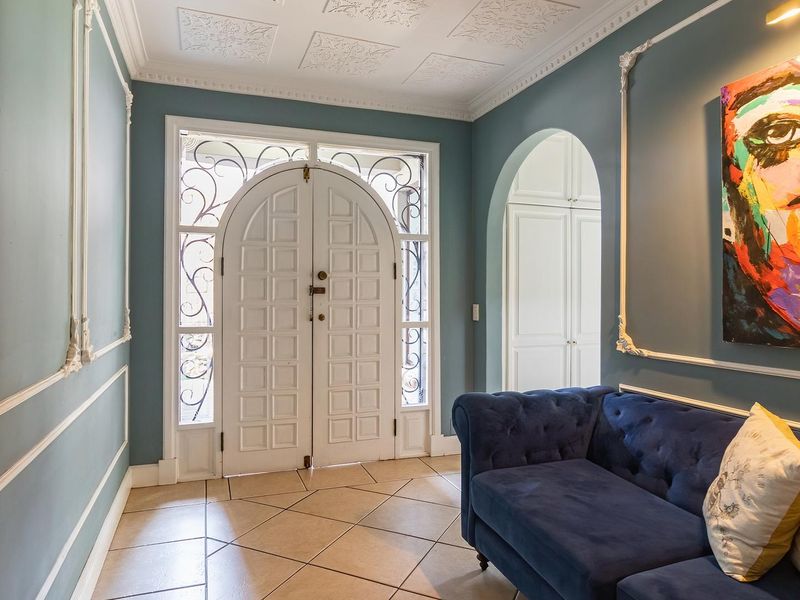 Elegant entrance hall featuring decorative ceiling tiles, crown molding, wall paneling, tiled flooring, and a secure double front door with wrought iron detailing.