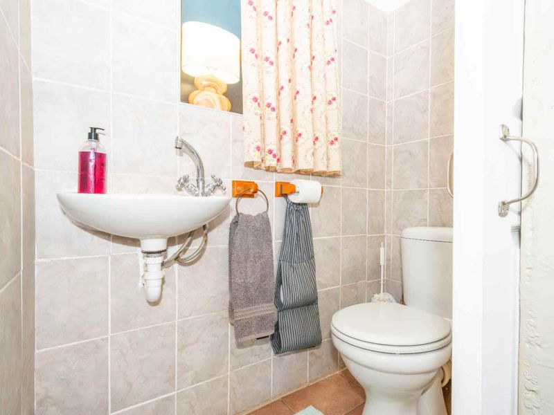 A compact bathroom featuring tiled walls, a wall-mounted basin, and a standard toilet.