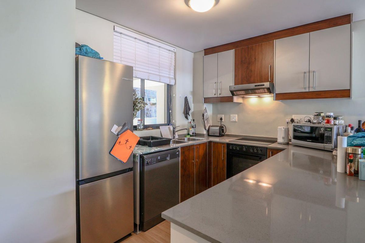 Modern kitchen featuring wood-grain and light-toned cabinetry, stone countertops, integrated oven, hob, and extractor fan, with a functional layout and stainless steel finishes.