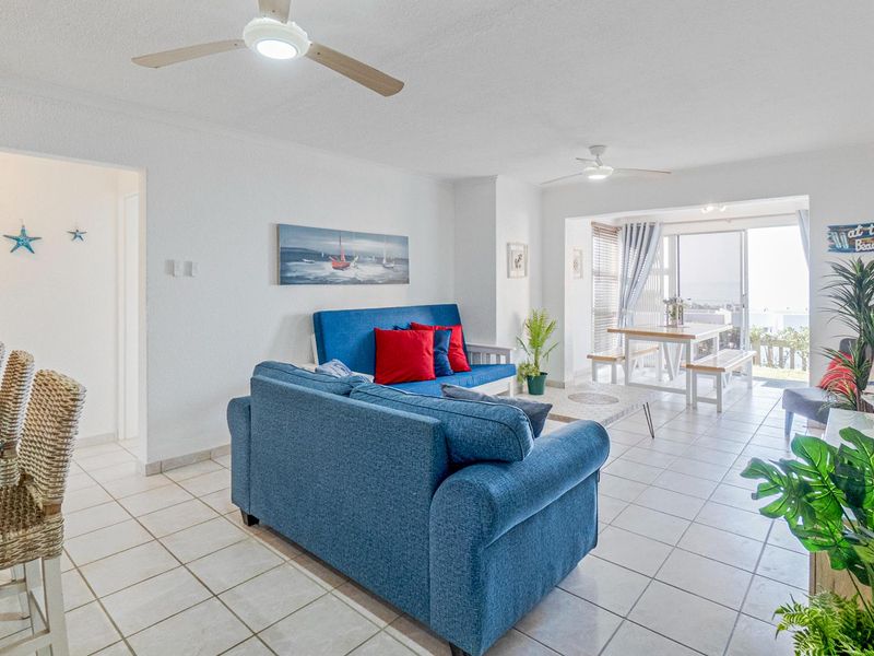 Open-plan living and dining area featuring tiled flooring, ceiling fans, and sliding glass doors leading to an outdoor space with coastal views.